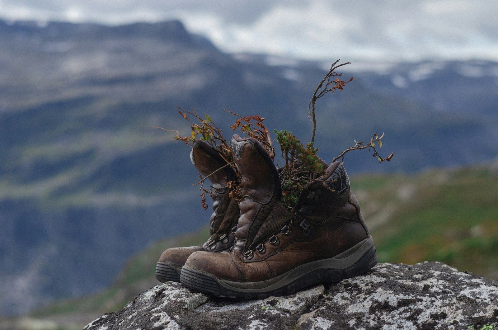 A pair of worn brown leather hiking boots on a rock above a Norwegian valley.