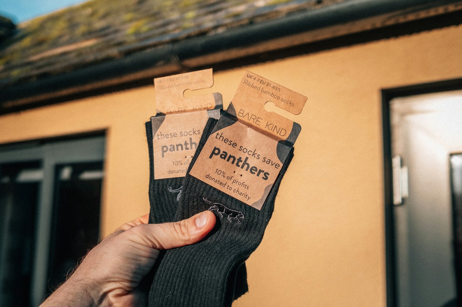 A hand holding a pair of dark hiking socks outside a cabin.